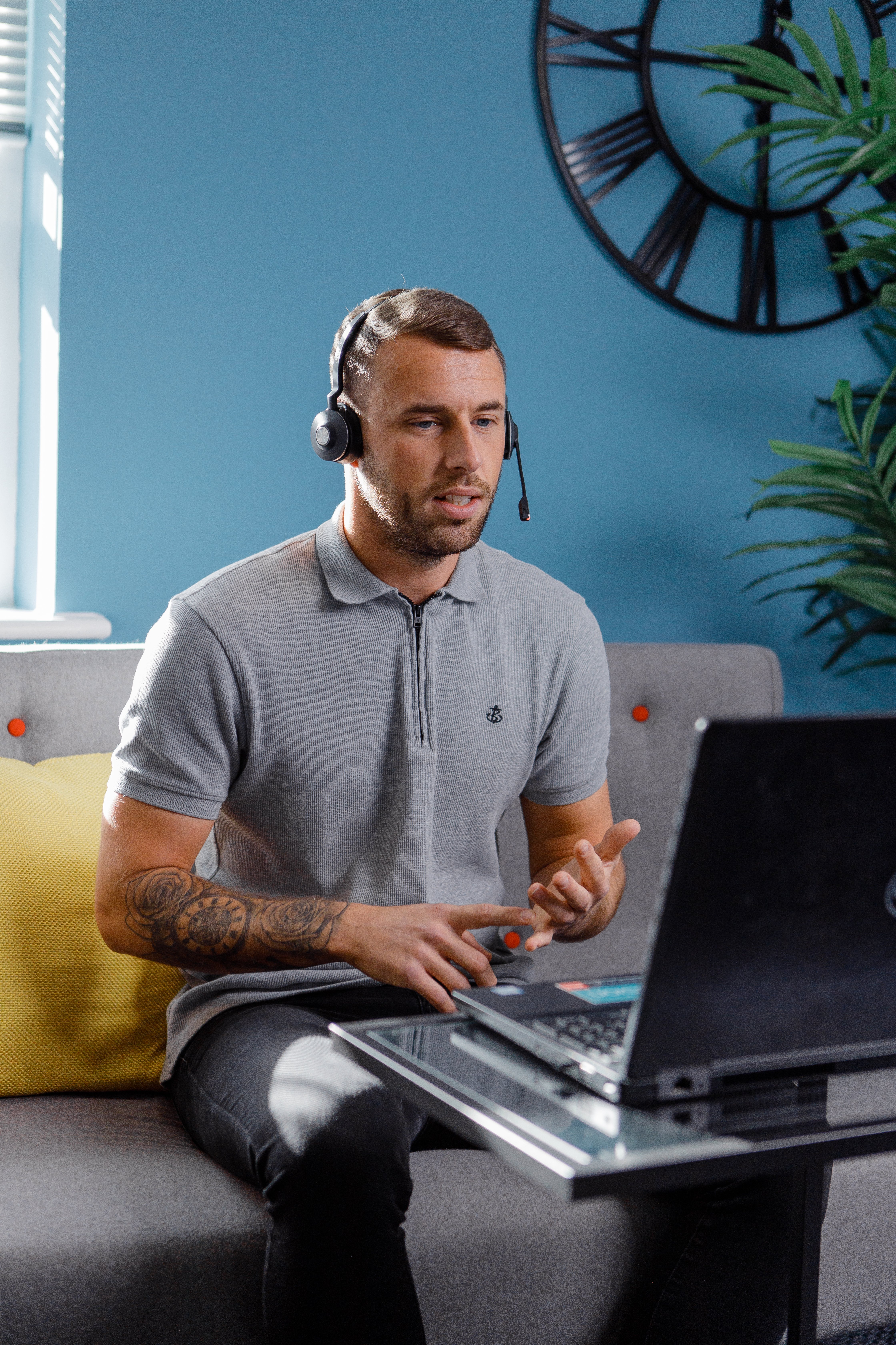 Man in a grey shirt and headset sitting in front of his laptop and speaking to a customer 