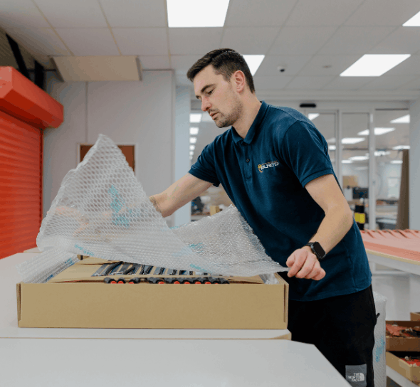 A man in a blue polo shirt covering a box with bubble wrap