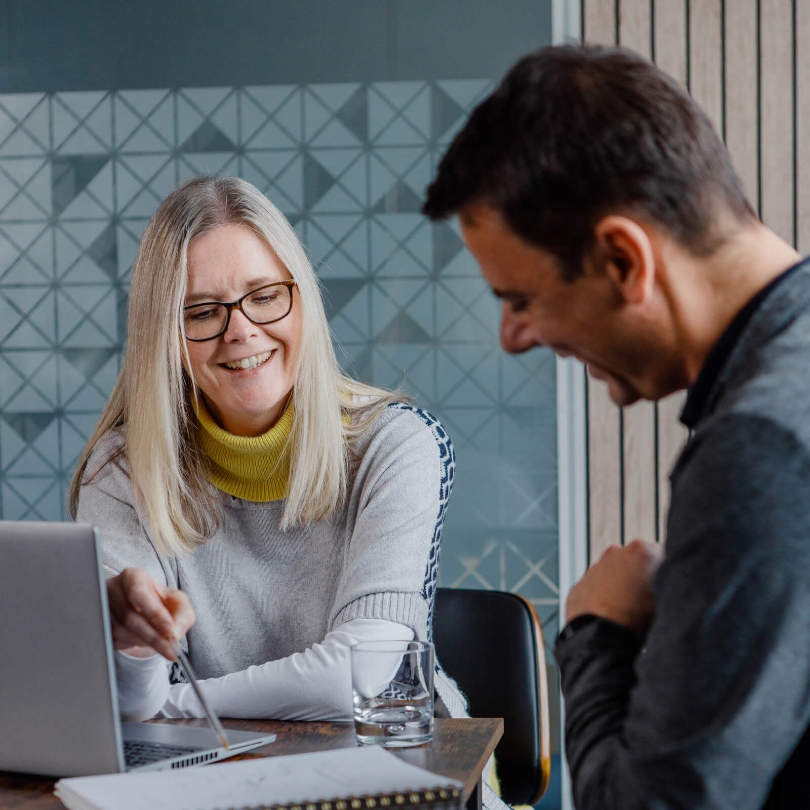 Smiling male and female colleagues sitting at a desk and reviewing data on a laptop screen 