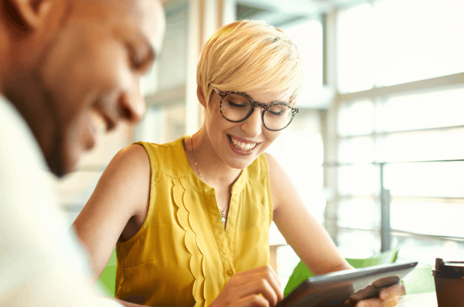 A woman with glasses smiling whilst looking down at a tablet