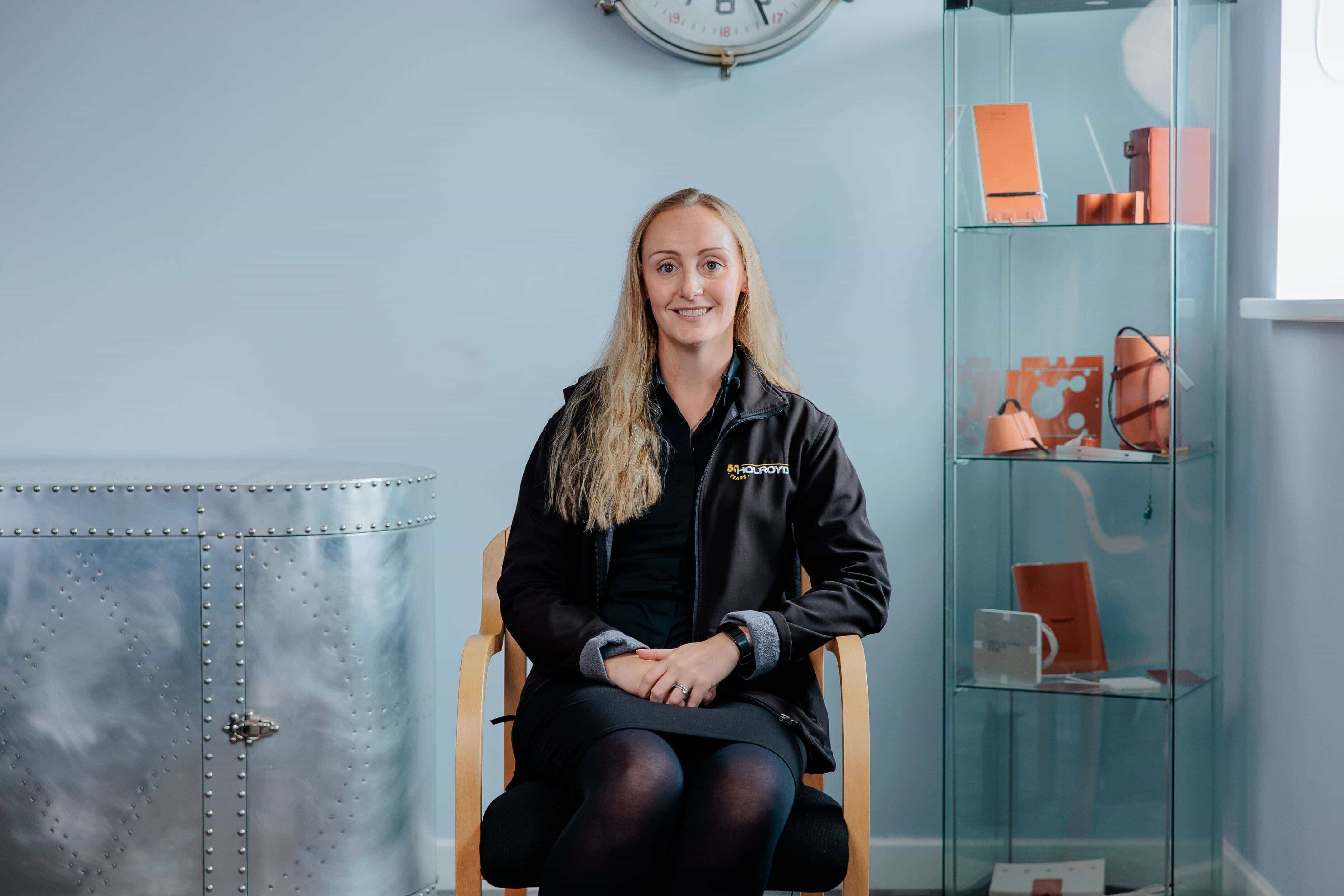 A woman with long blonde hair sat on a chair smiling
