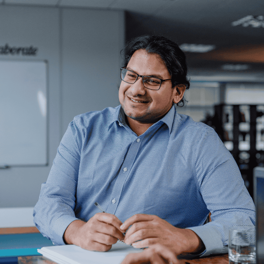 A man smiling whilst holding a pen to a notepad